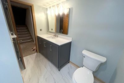 Bathroom view showing gray vanity, mirror, toilet, and tiled floor