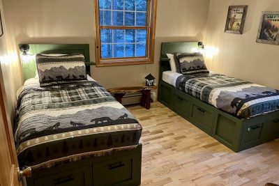 Two single beds with dark green storage drawers underneath, set in a room with light walls, decorated with wildlife-themed bedding