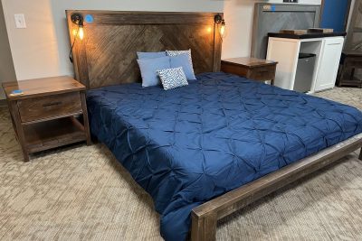 A contemporary bedroom showcasing a large wooden bed frame with a blue comforter, flanked by matching wooden side tables with wall-mounted lamps