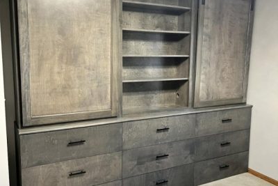 A large gray wooden dresser with sliding barn-style doors on top revealing shelving, and multiple drawers below