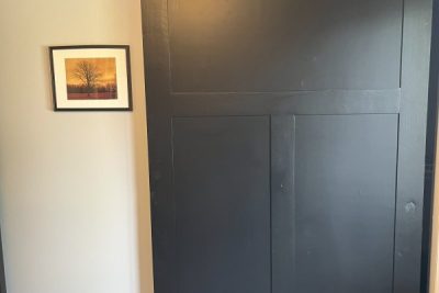 A closed black sliding barn door with metal hardware next to a framed picture on a wall
