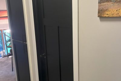 Double black panel doors slightly ajar, leading into a brightly lit room with a picture hanging nearby