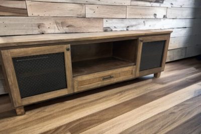 Wooden TV stand with decorative mesh doors against a rustic wood plank wall