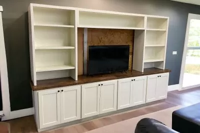 White built-in entertainment center with dark wood top and shelves beside a TV