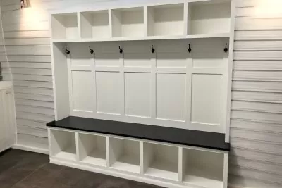 Mudroom bench integrated into a wall having black shelf and hooks.