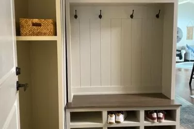 Mudroom bench with hooks having shoes in the lower section and a shelf to its left 