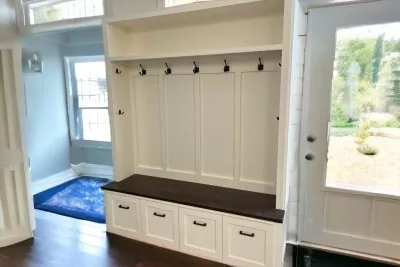 White mudroom hall tree with a black shelf and hooks in a bright hall