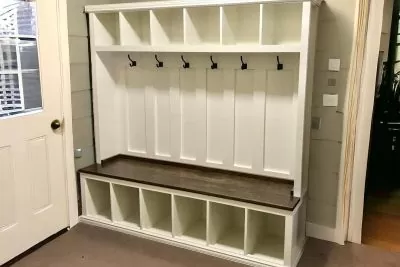 A white hall tree with a wooden shelf and hooks in a room having brown floor and a door