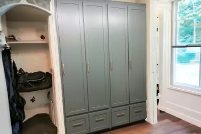 Gray mudroom locker with doors and a luggage shelf to its left in a room with a wooden floor