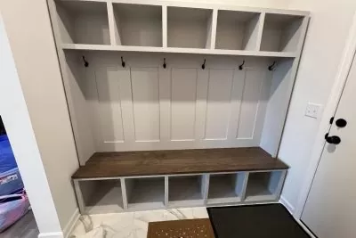 A clean and empty built-in mudroom bench with hooks, bench seating, and cubbies, situated near a door.