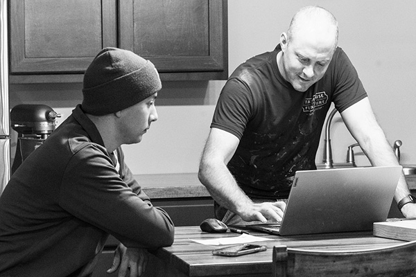 Two men collaborating at a laptop in a kitchen