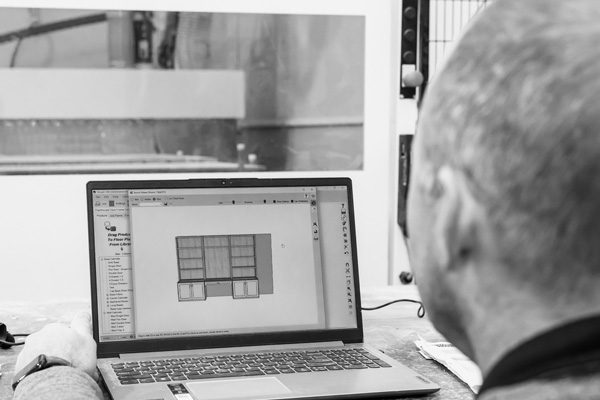 Man reviewing furniture design on a laptop in a woodworking shop