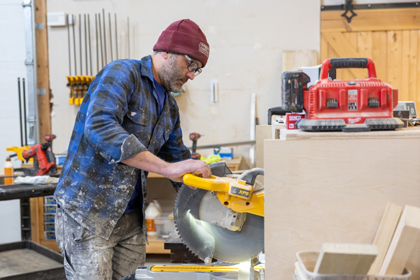 JWAT2943 Carpenter cutting wood on a miter saw in a workshop